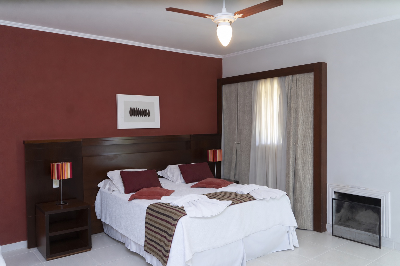 Interior do chalé com cama de casal, cortina e lareira